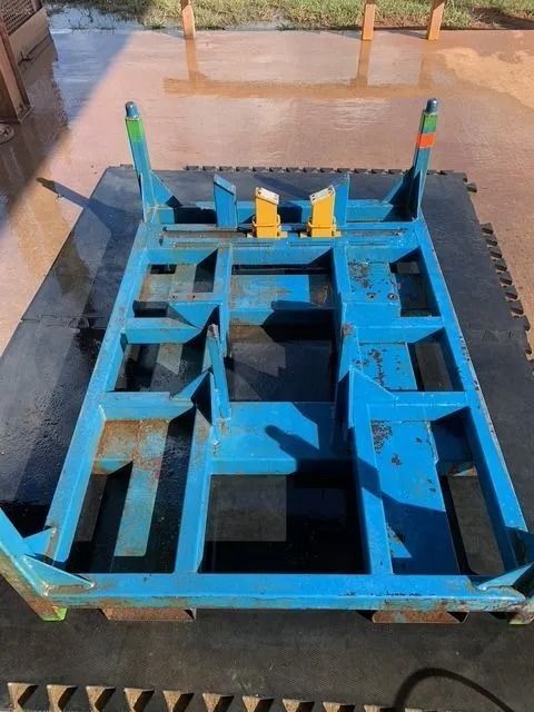 Blue metal frame cart on a black mat, with yellow wheel chocks. Outdoors on concrete.