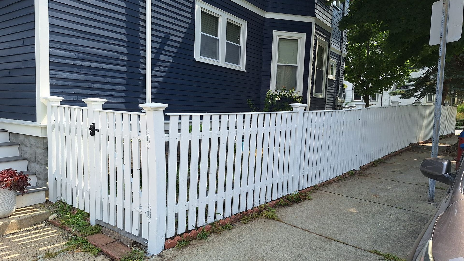 White picket fence in front of a blue house, sidewalk on right.