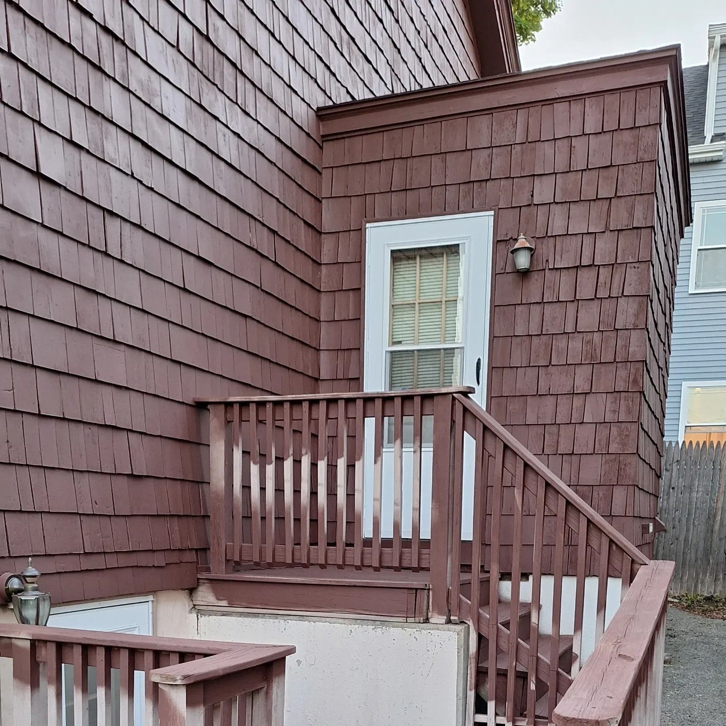 Brown shingle-sided building with a doorway, wooden stairs, and railing.