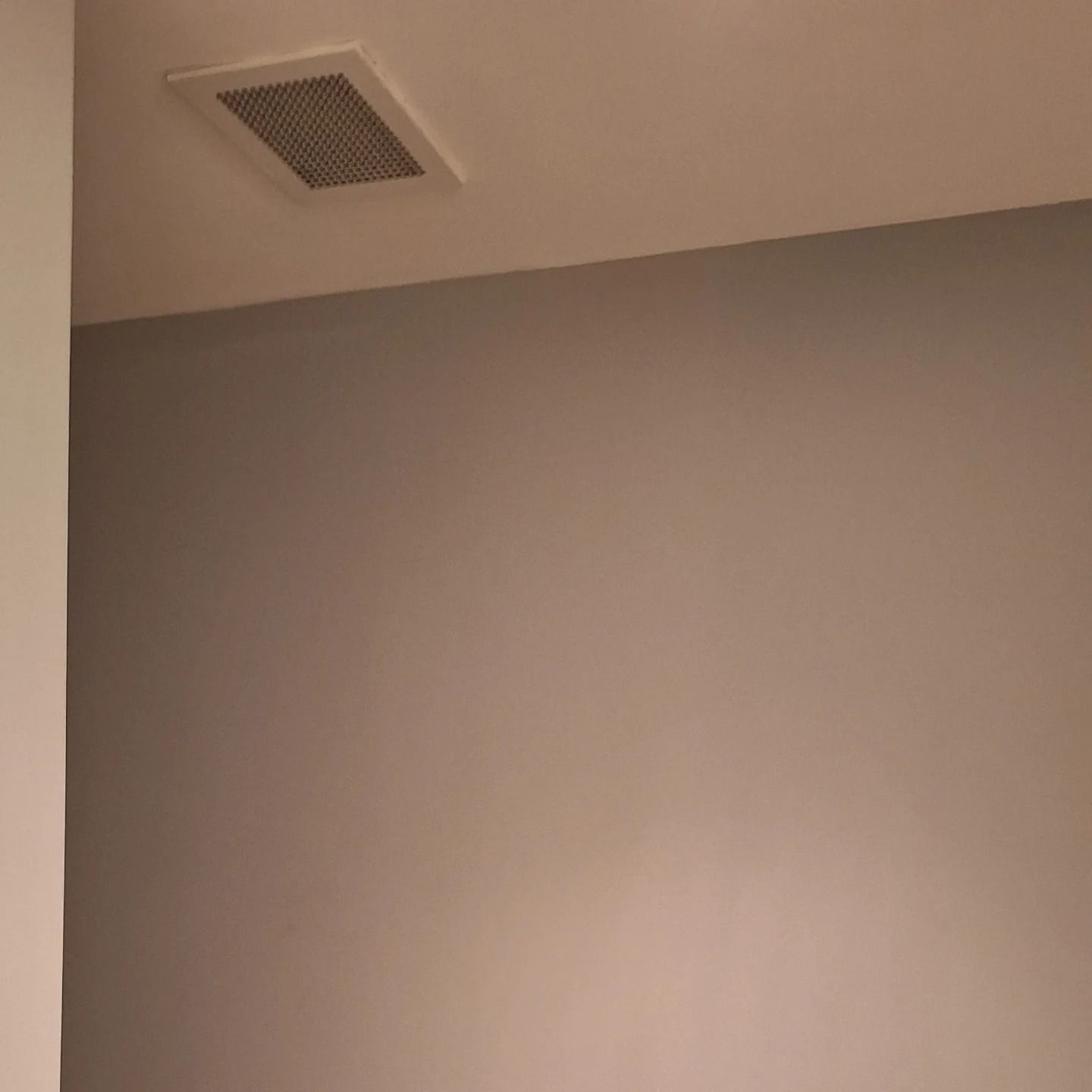 Ceiling vent in a room with a light gray wall. A white wall is in the left corner.