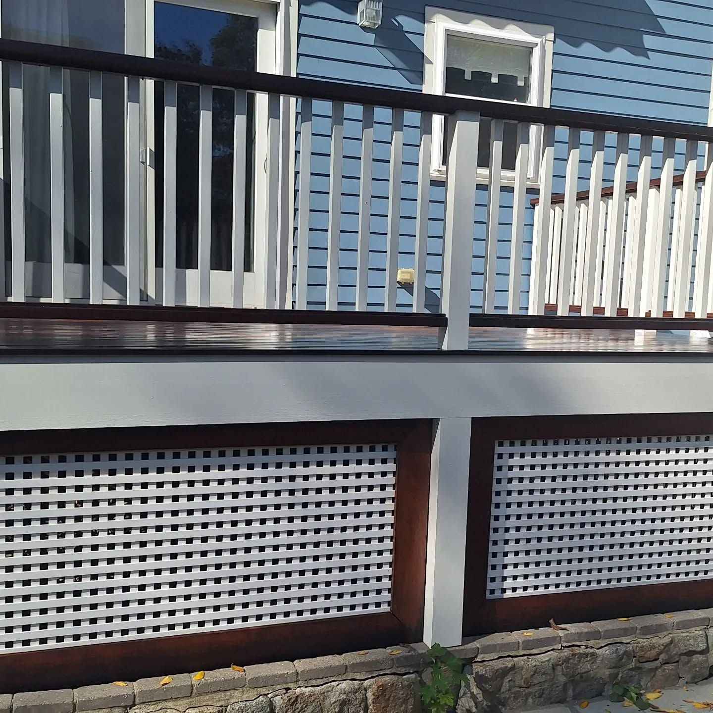 Blue house with a white deck railing and lattice skirting.