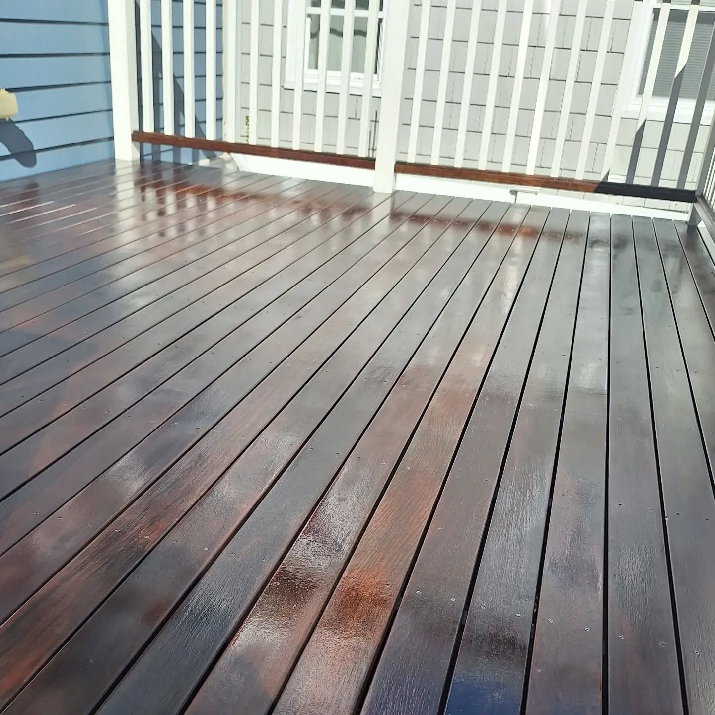 Newly stained wooden deck with shiny, dark brown planks. White railing and light blue siding in background.
