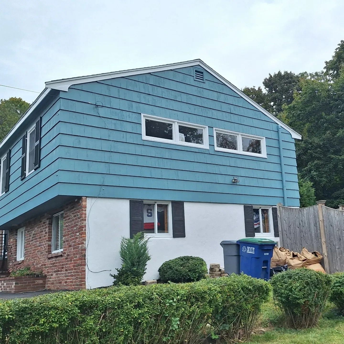 Two-story house with blue siding on the upper level and white paint over brick on the lower level.