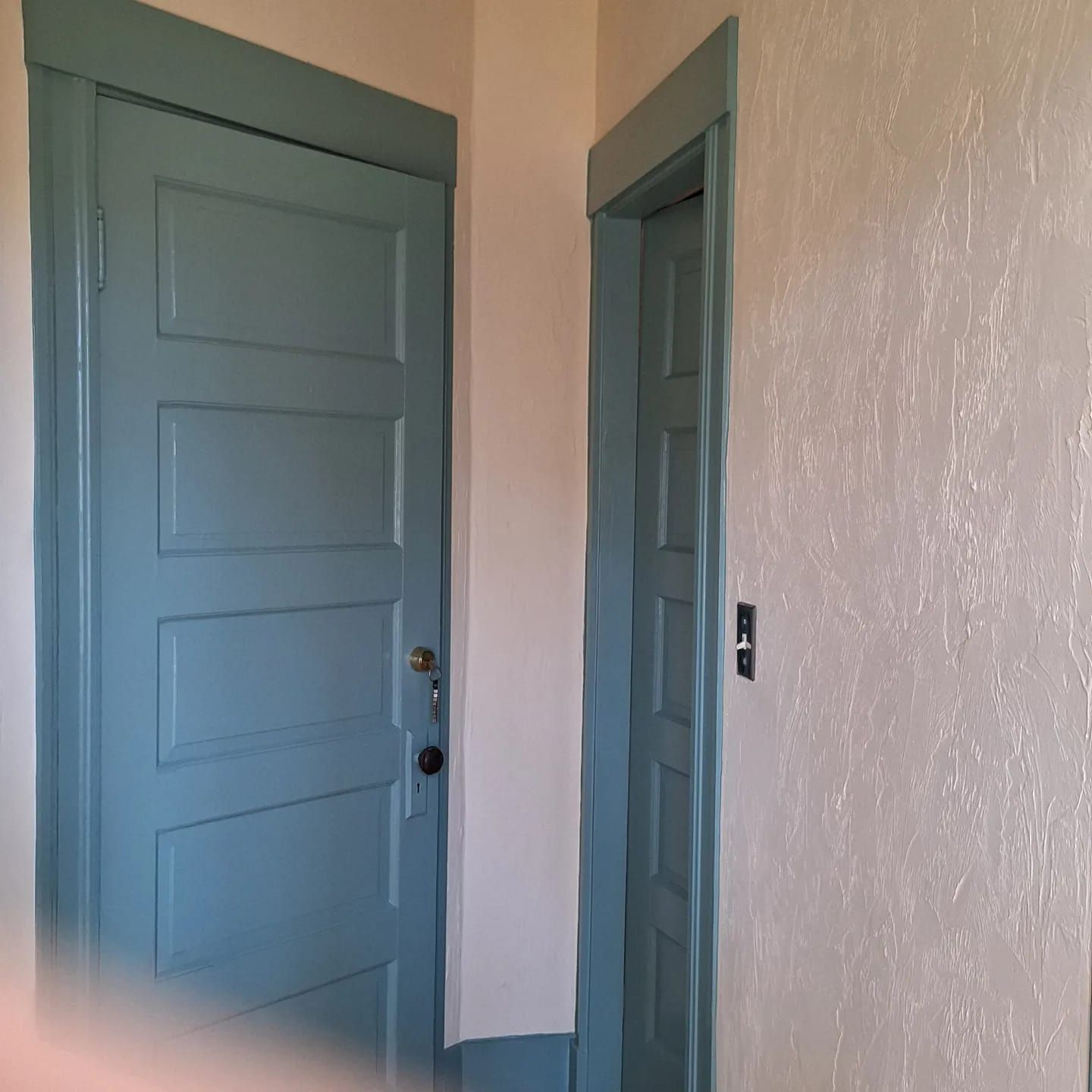Two blue doors in a hallway with textured white walls.
