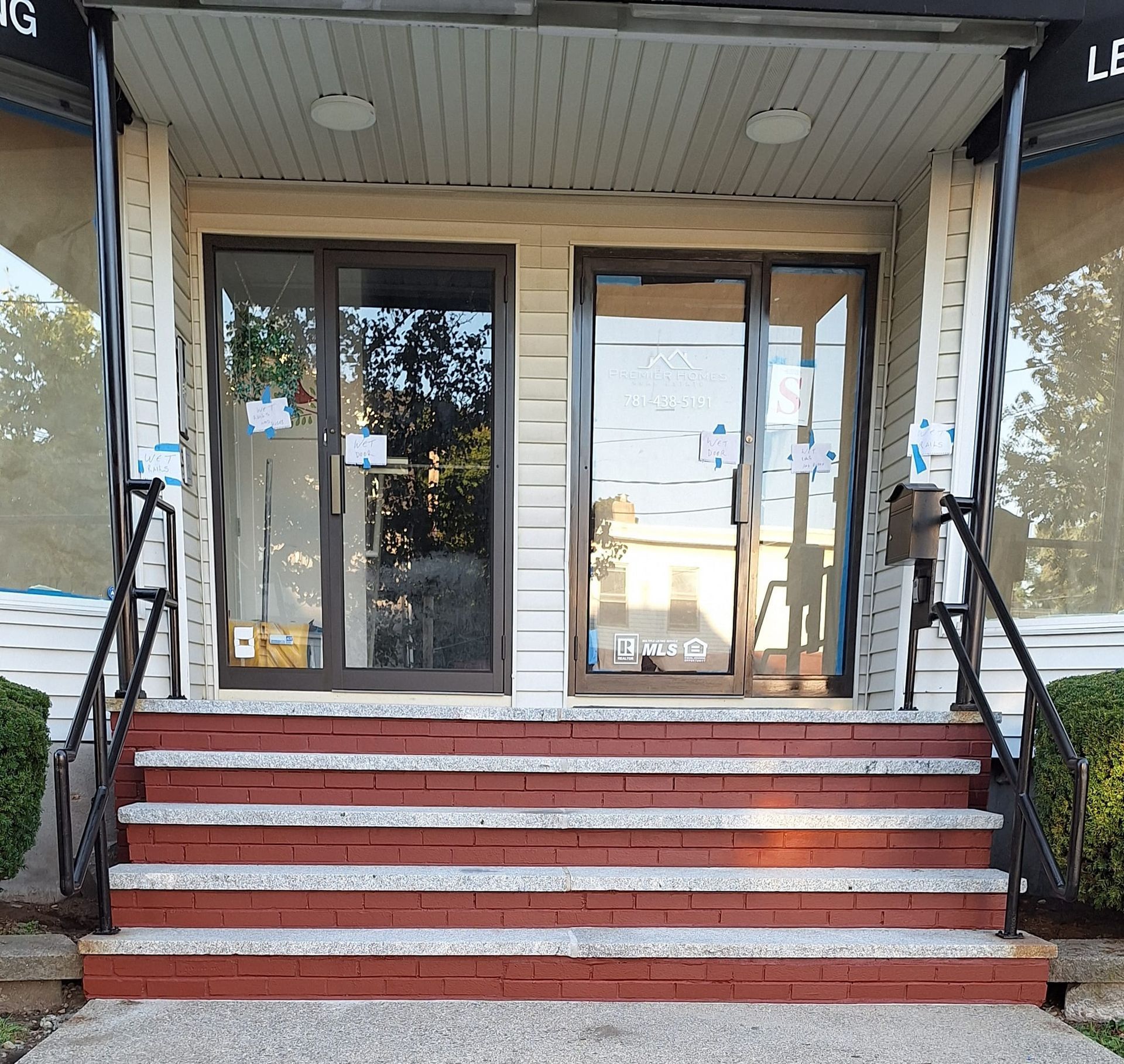 Exterior of a building with two glass doors, brick steps, and a black handrail.