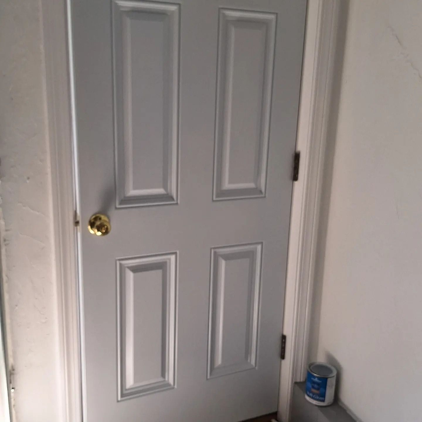 Gray door with four rectangular panels, gold doorknob, and a can of blue paint.