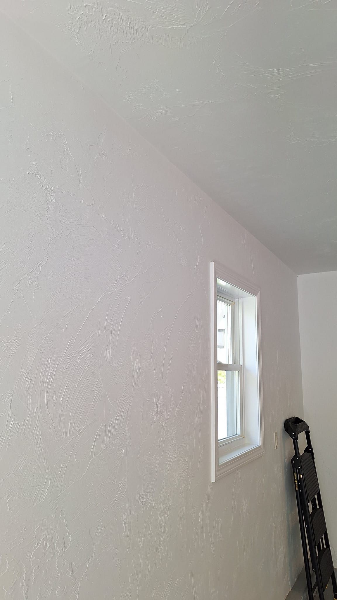 White wall with small window and ladder in corner. Textured ceiling and walls.