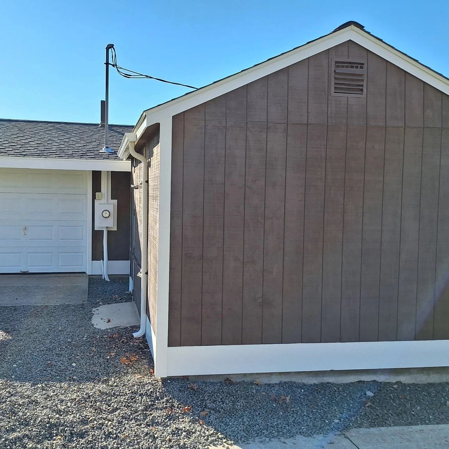 Brown wooden shed with white trim next to a white garage. Blue sky.
