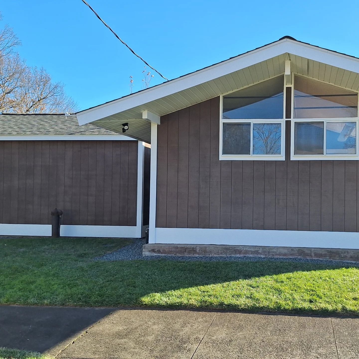 Brown house with white trim, a small grassy lawn, and a clear blue sky.