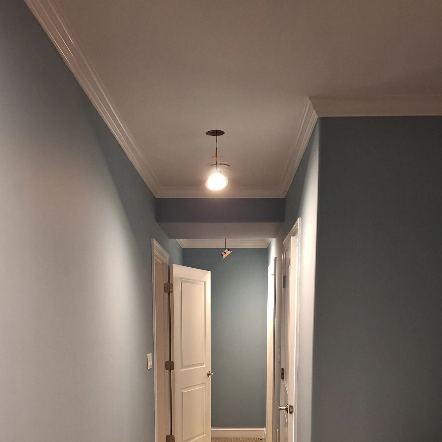 Blue hallway with white trim, doors, and a hanging light fixture.