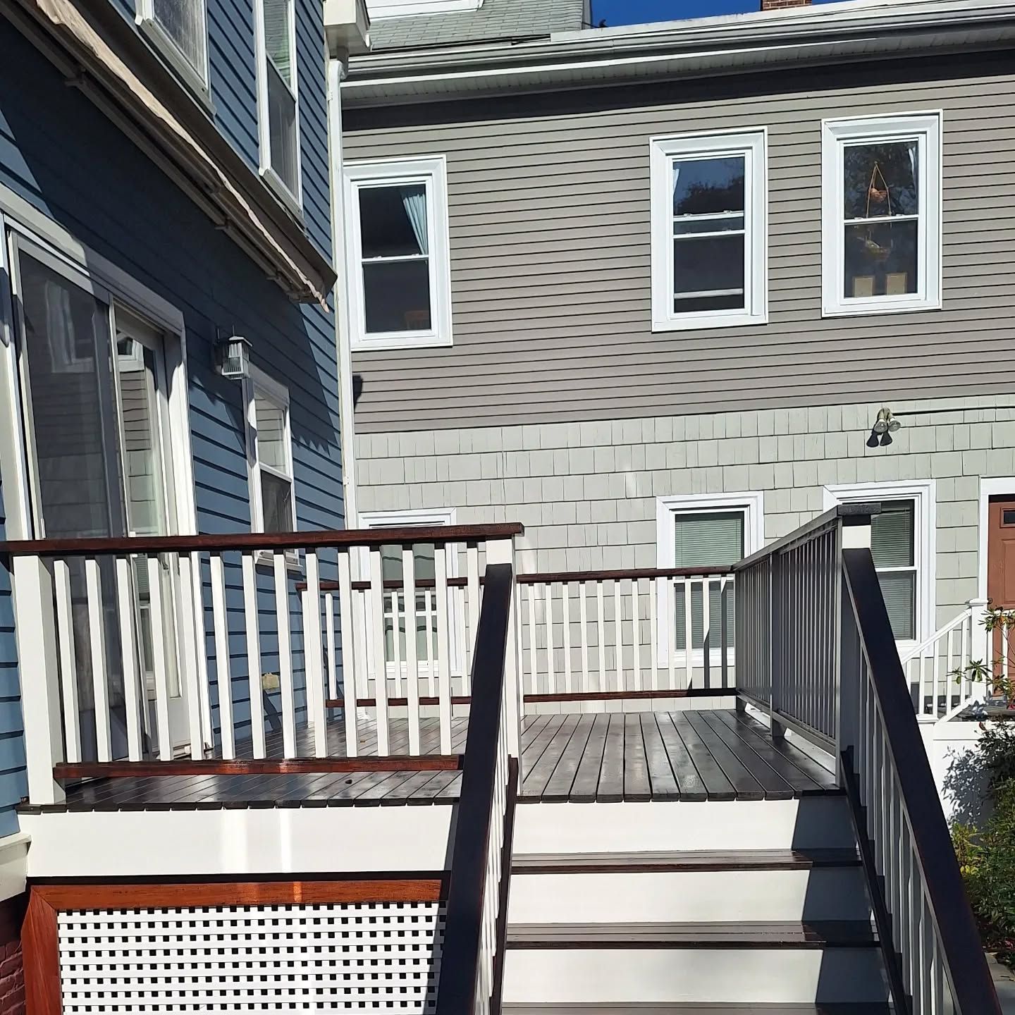 Wooden deck and stairs leading to a building with blue and gray siding; sunny day.