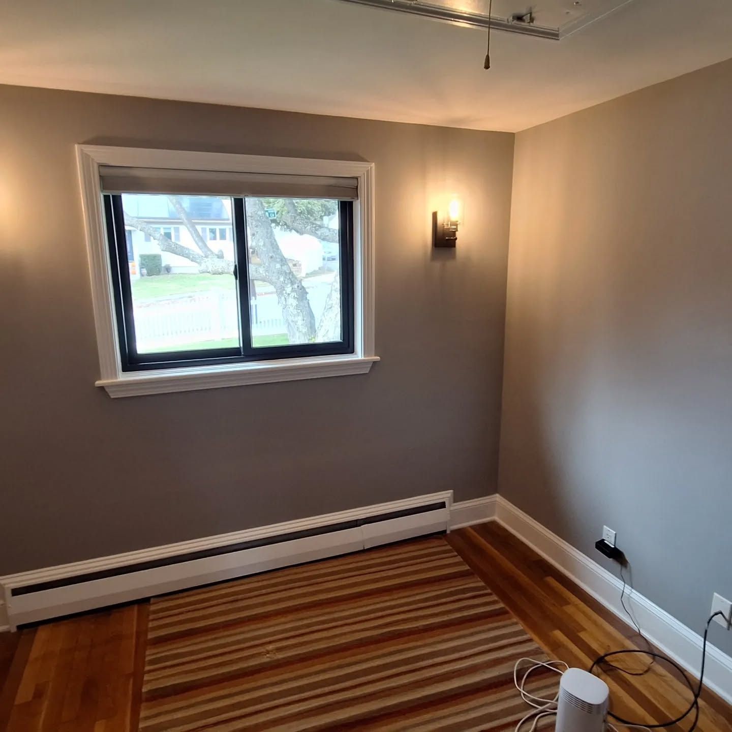 Empty bedroom with gray walls, window, radiator, hardwood floor and striped rug.