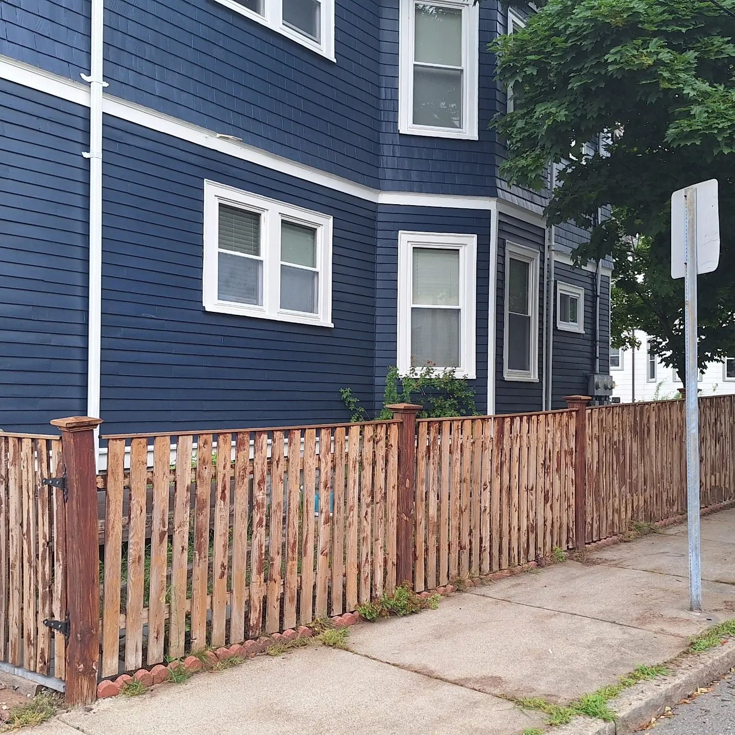 Blue house with white-framed windows, brown wooden fence along the sidewalk, and a street sign.