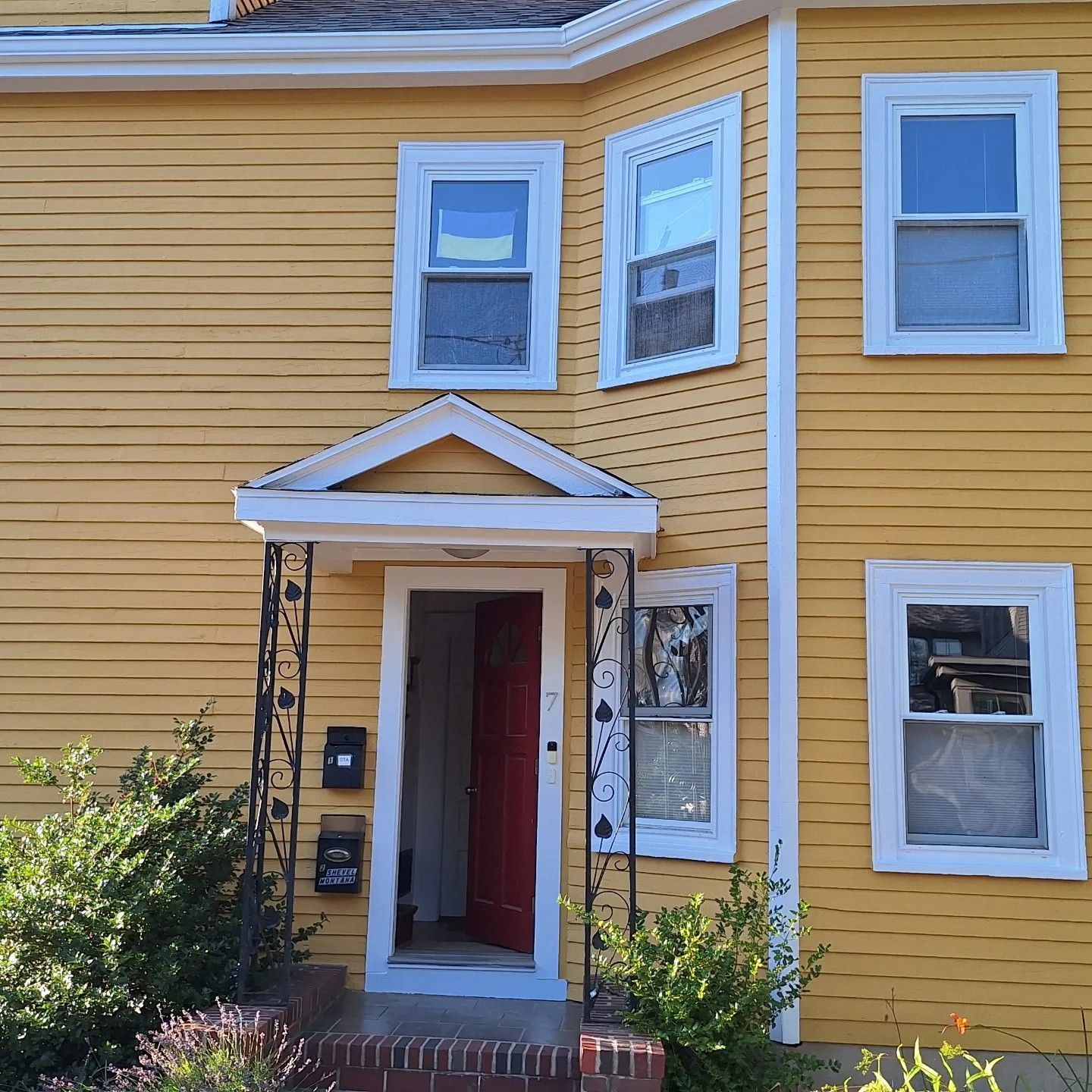 Yellow house with white trim, red door, and multiple windows.