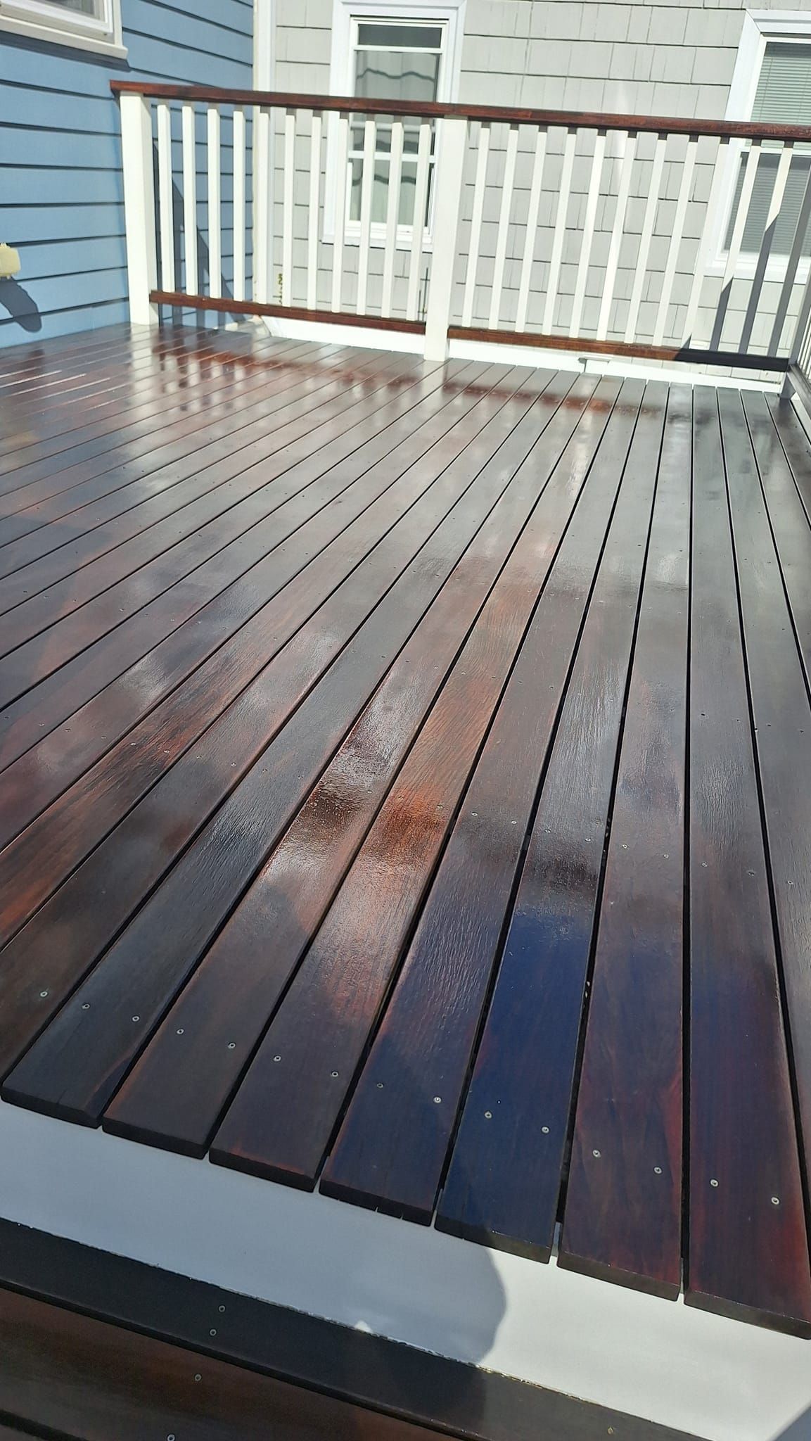 Wet, stained wooden deck with white railing against a light gray building.