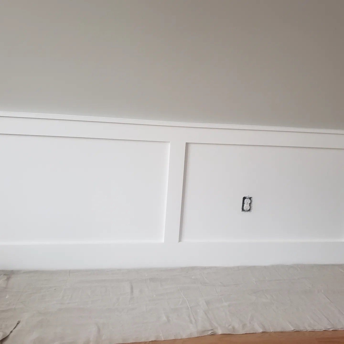 White wainscoting on a wall with a ceiling and an electrical outlet.