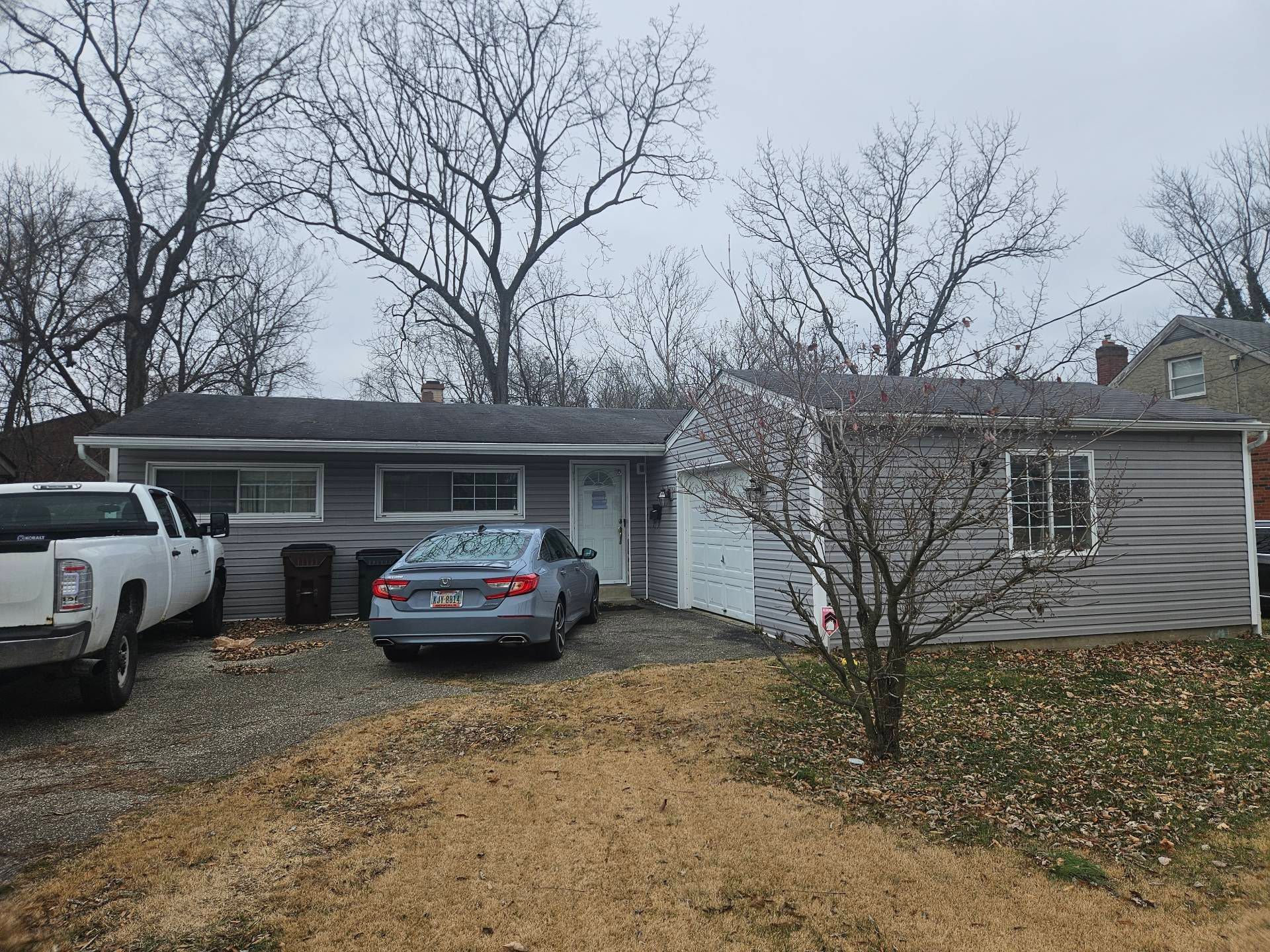 Single-story house with two parked cars, a gravel driveway, and bare trees in front.