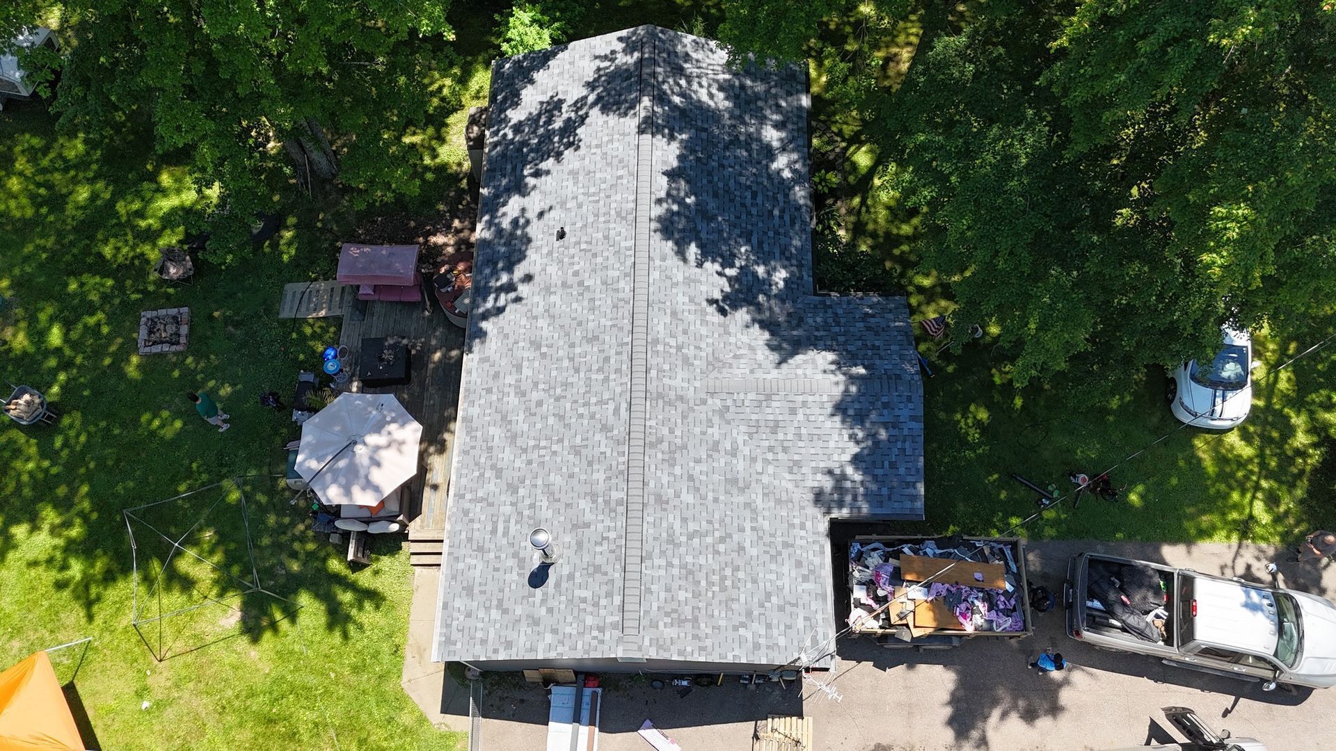 Aerial view of a large gray-roofed building with trees and parked vehicles around it.