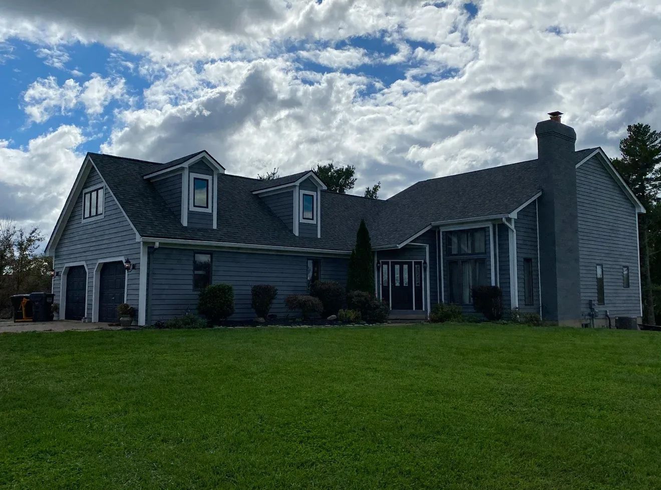 Large gray house with dormer windows and a green lawn under a cloudy sky