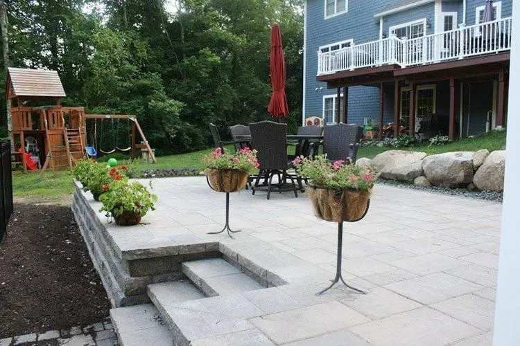 Stone patio with steps, flower baskets, dining set, and a play structure.