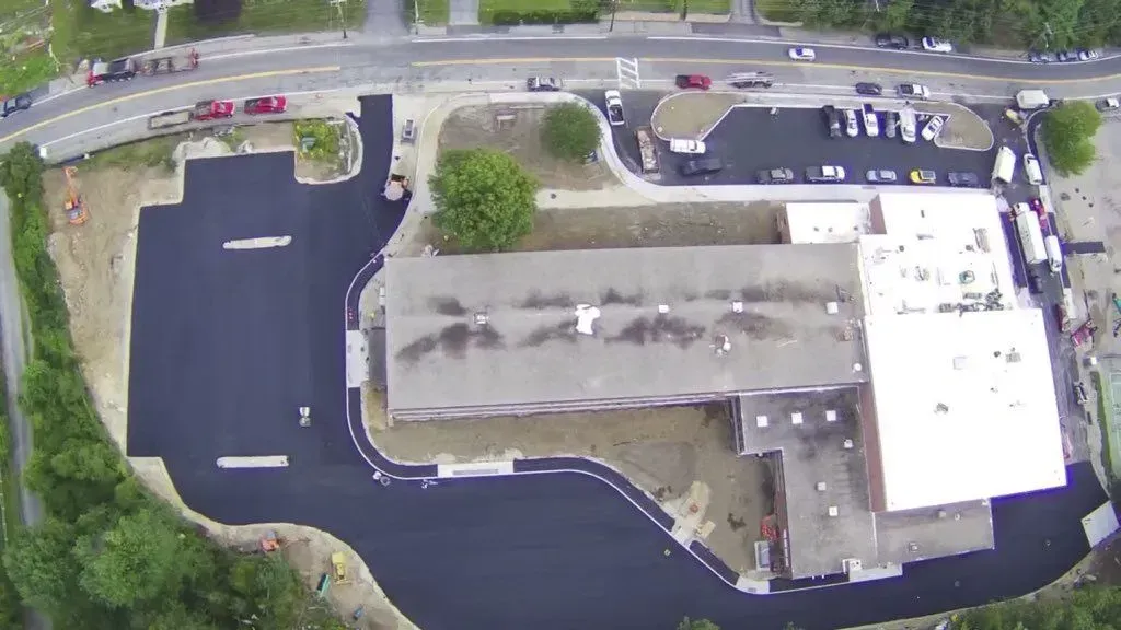Aerial view of a building with a dark asphalt lot, and a nearby road with vehicles.