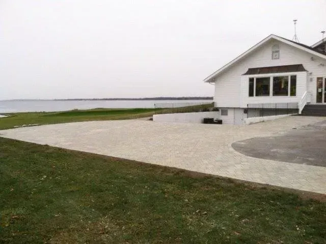 White building with large windows overlooking a body of water and a paved parking area on a cloudy day.