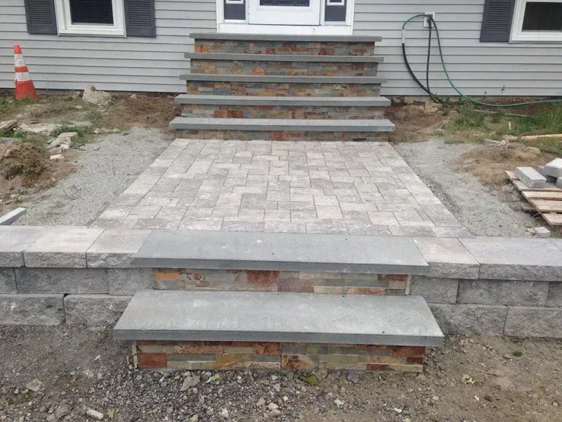Stone steps and walkway leading to a house entrance; gray and brown stone materials; construction setting.