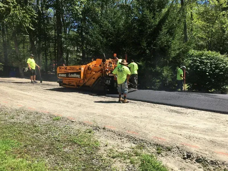 Road paving crew laying asphalt; orange paving machine, green shirts.
