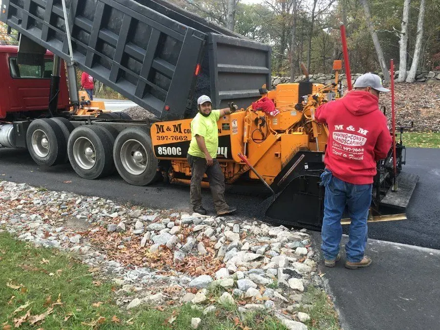 Asphalt paving with dump truck and two workers.