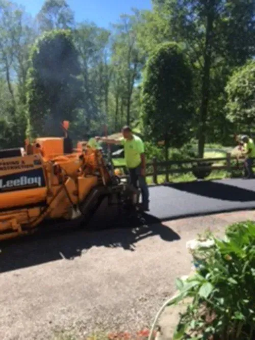 Workers paving a driveway with an asphalt machine on a sunny day.