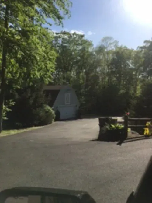 A driveway leads to a gray garage surrounded by trees on a sunny day.