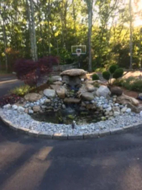 A decorative pond and waterfall feature surrounded by rocks and gravel, with a basketball hoop in the background.