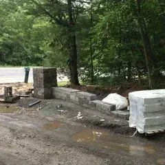 Stone retaining wall under construction next to a road, with materials and tools present.