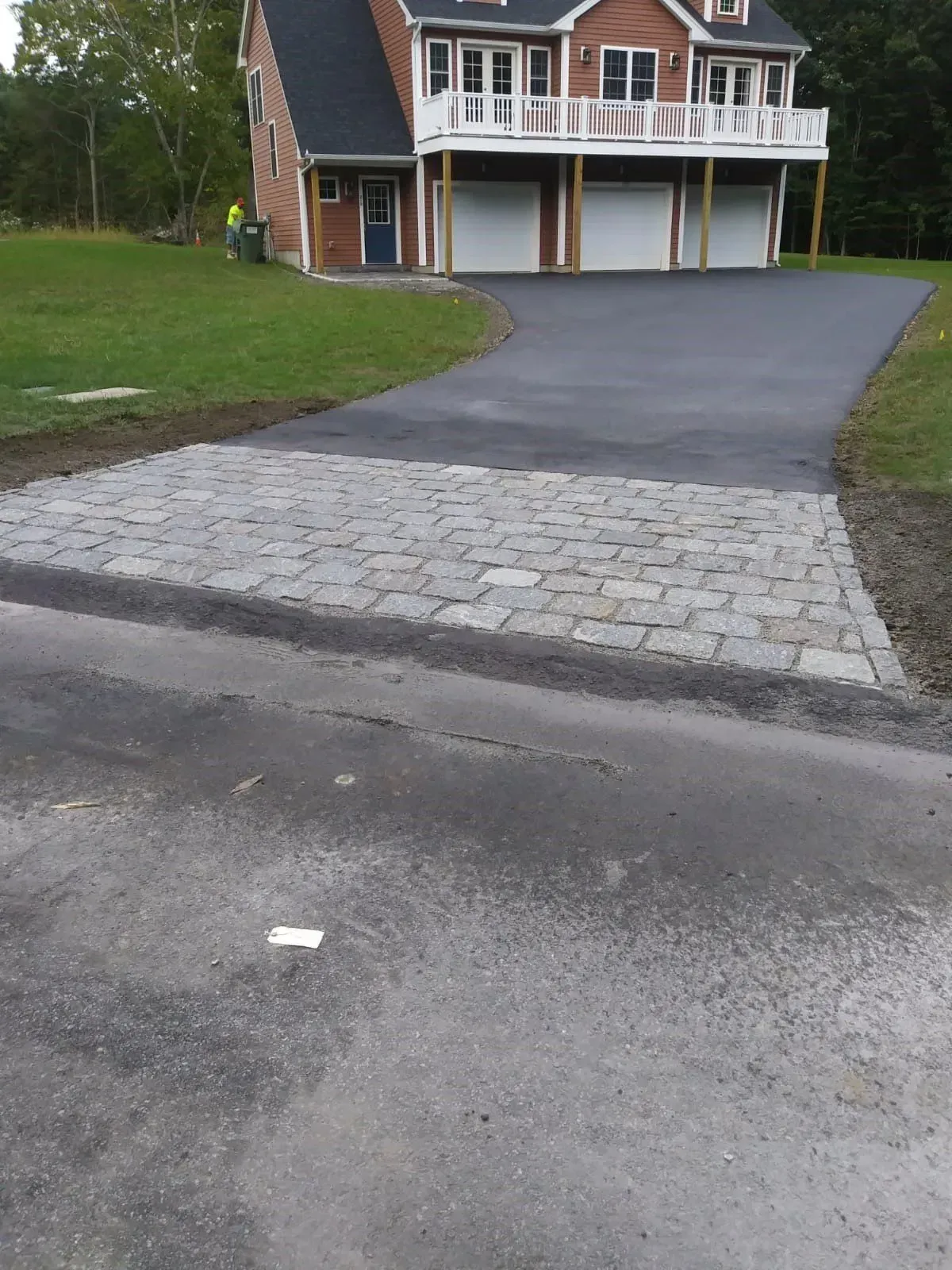 Asphalt driveway transitions to a brick paver apron in front of a house with a three-car garage.
