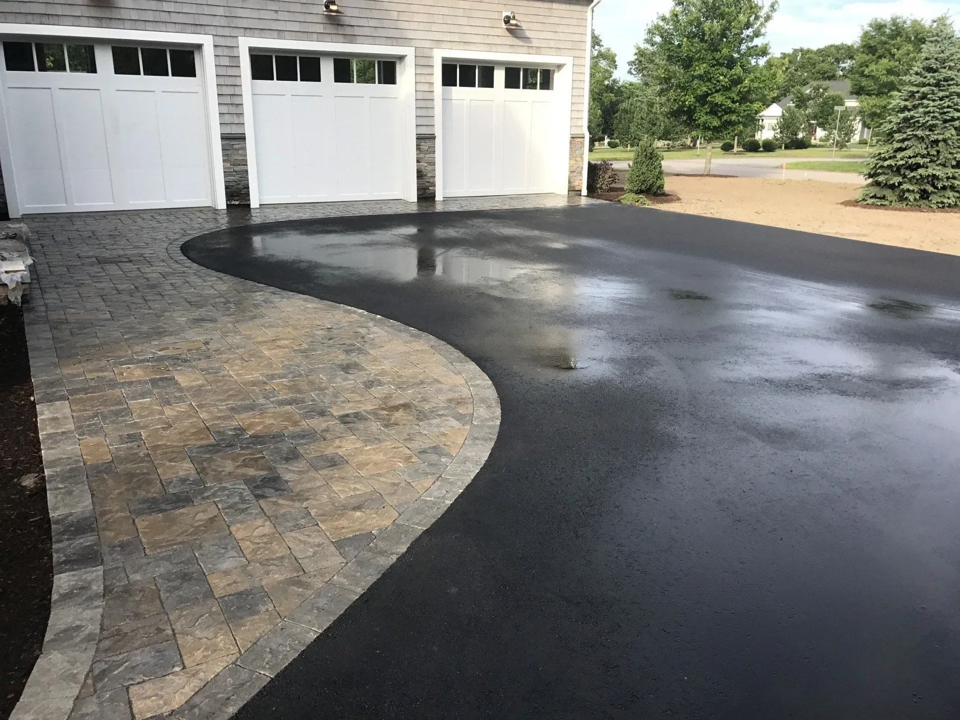 Driveway with brick walkway curving next to asphalt leading to a garage.