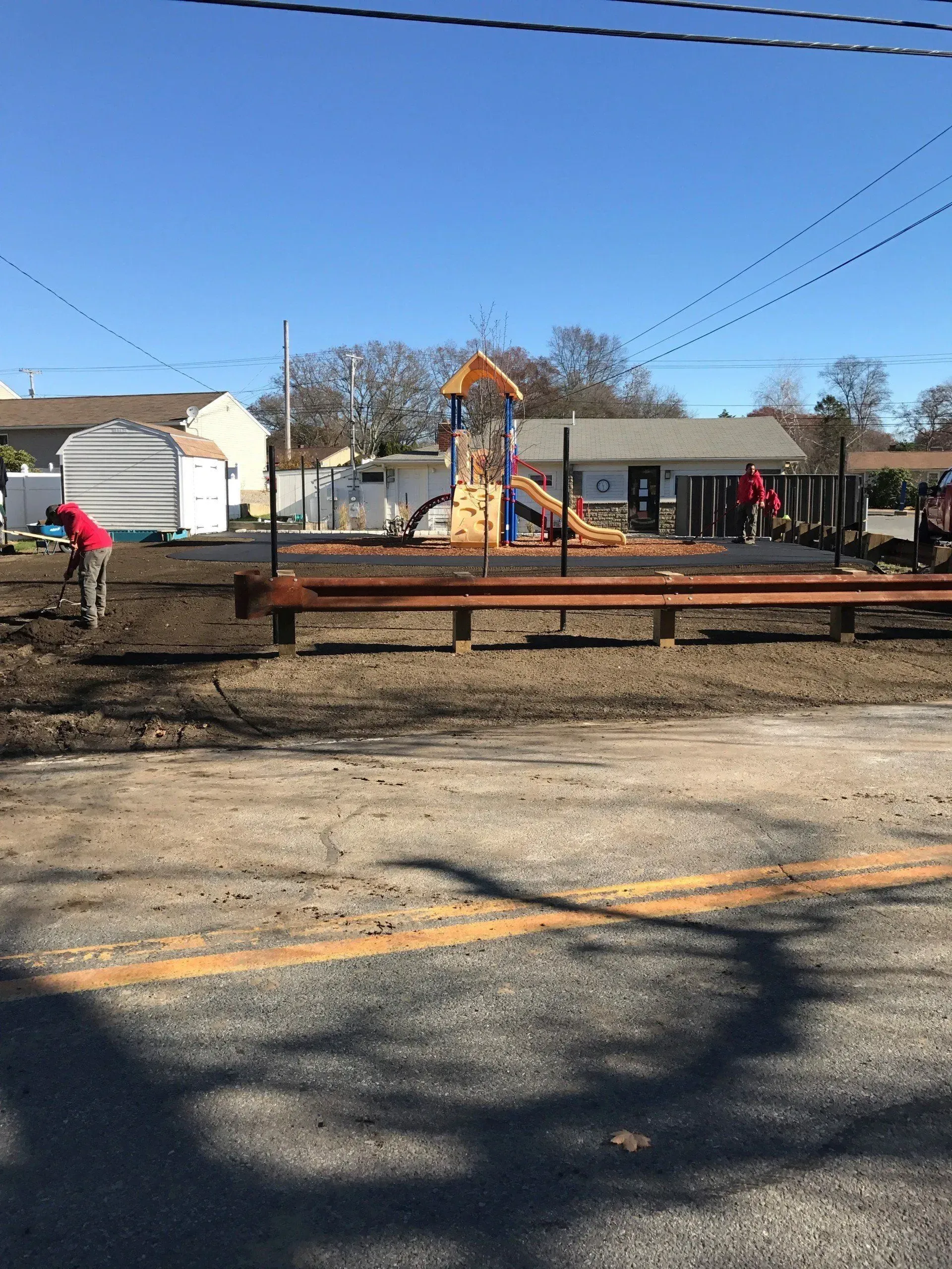 Workers at a playground. Preparing the ground near a wooden structure. Clear sunny day.