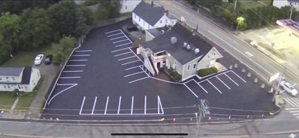 Aerial view of a parking lot next to a building and road, newly paved with parking space markings.