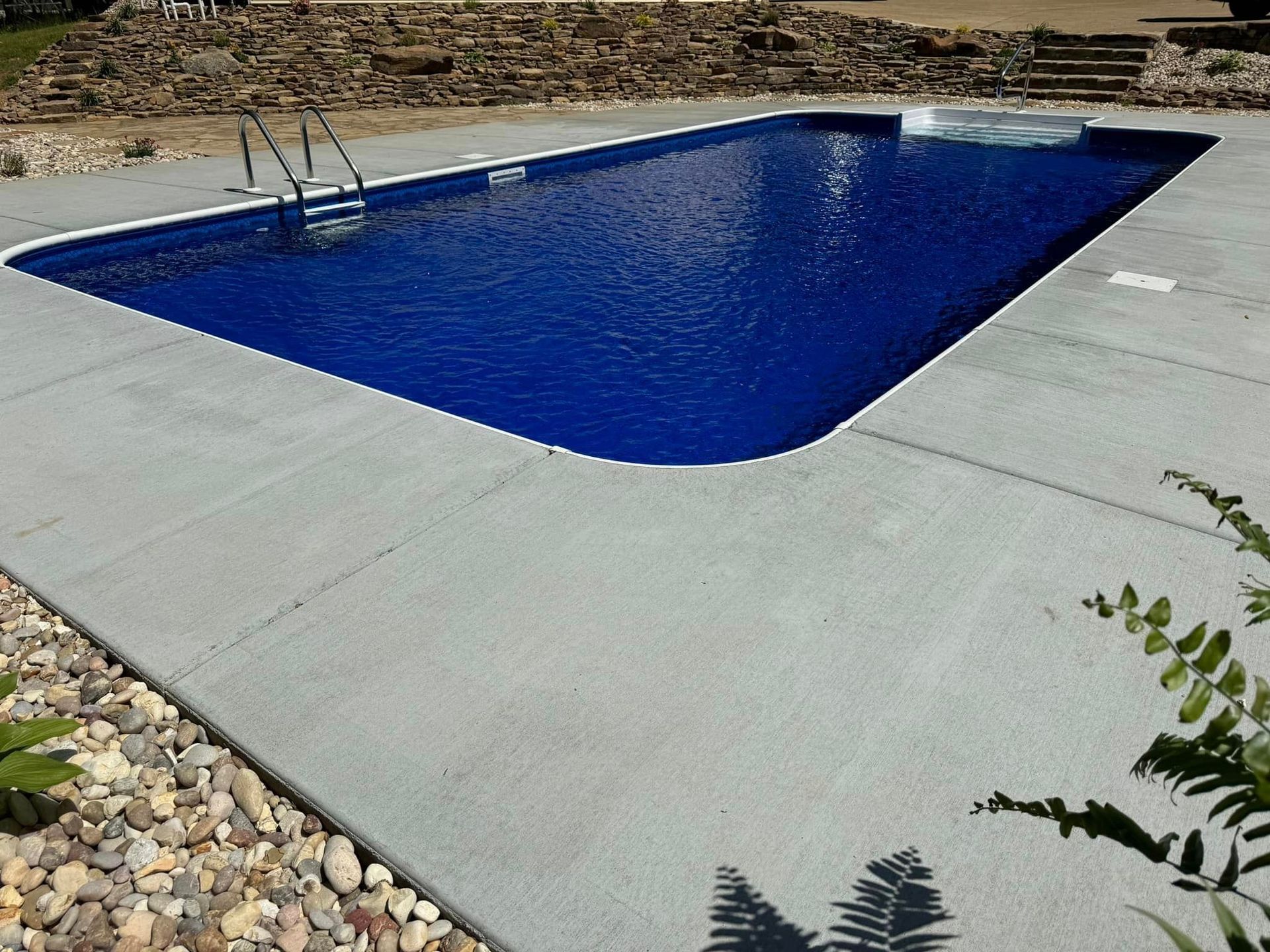 A large blue swimming pool is surrounded by rocks and concrete.