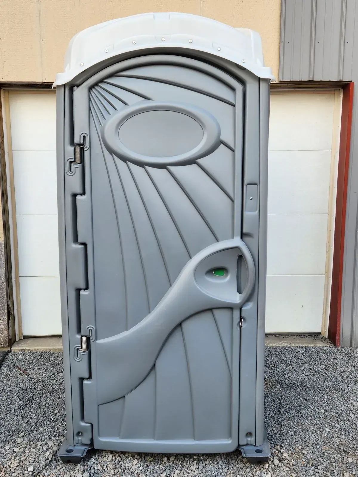 Gray portable toilet with white top, set against white garage door.