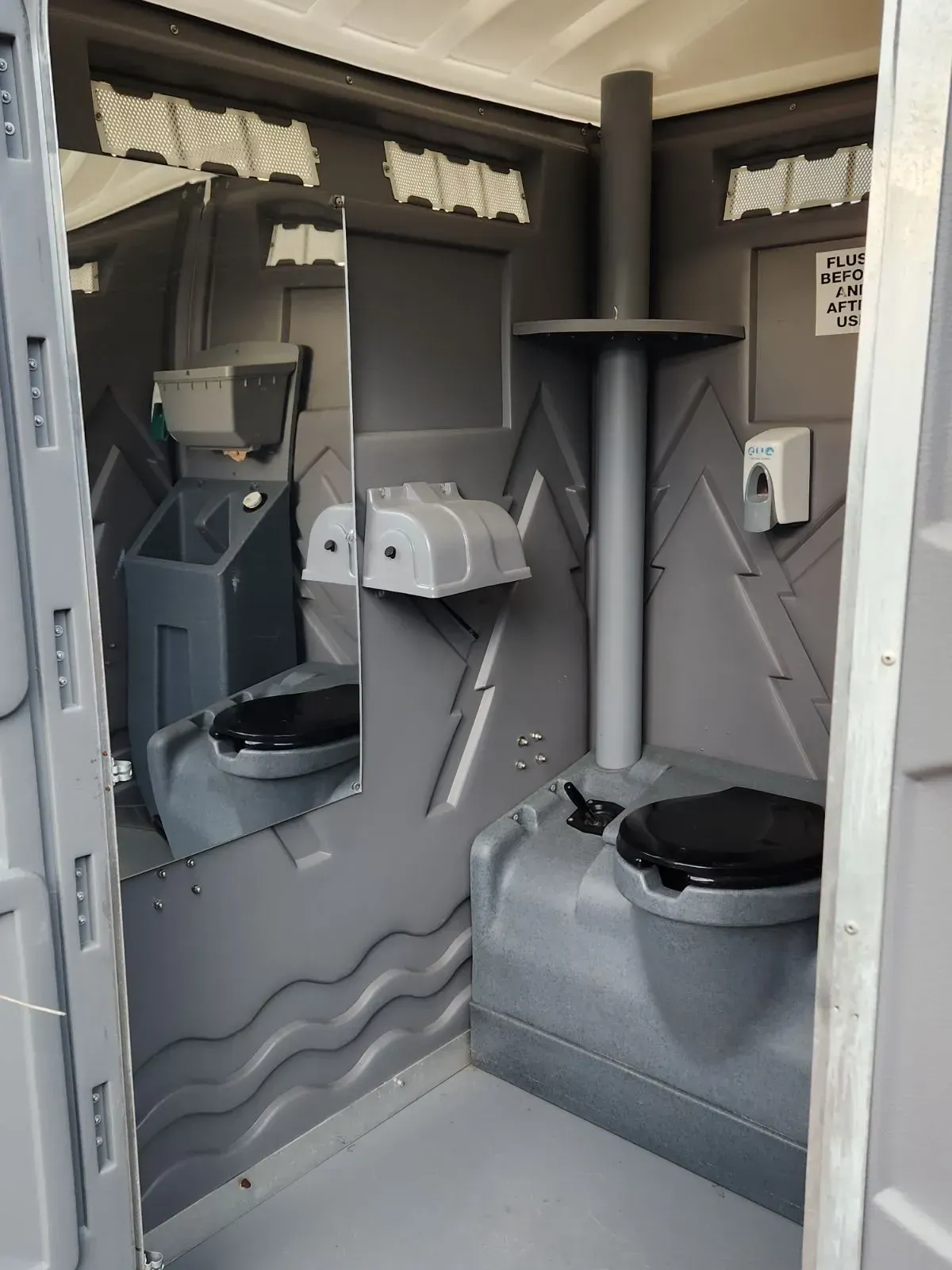 Interior of a gray portable toilet. Features include a toilet seat, mirror, soap dispenser, and ventilation.