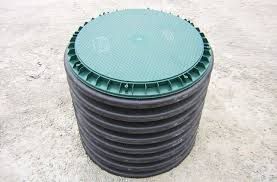 A green and black septic tank lid on a corrugated black tank, sitting outdoors.