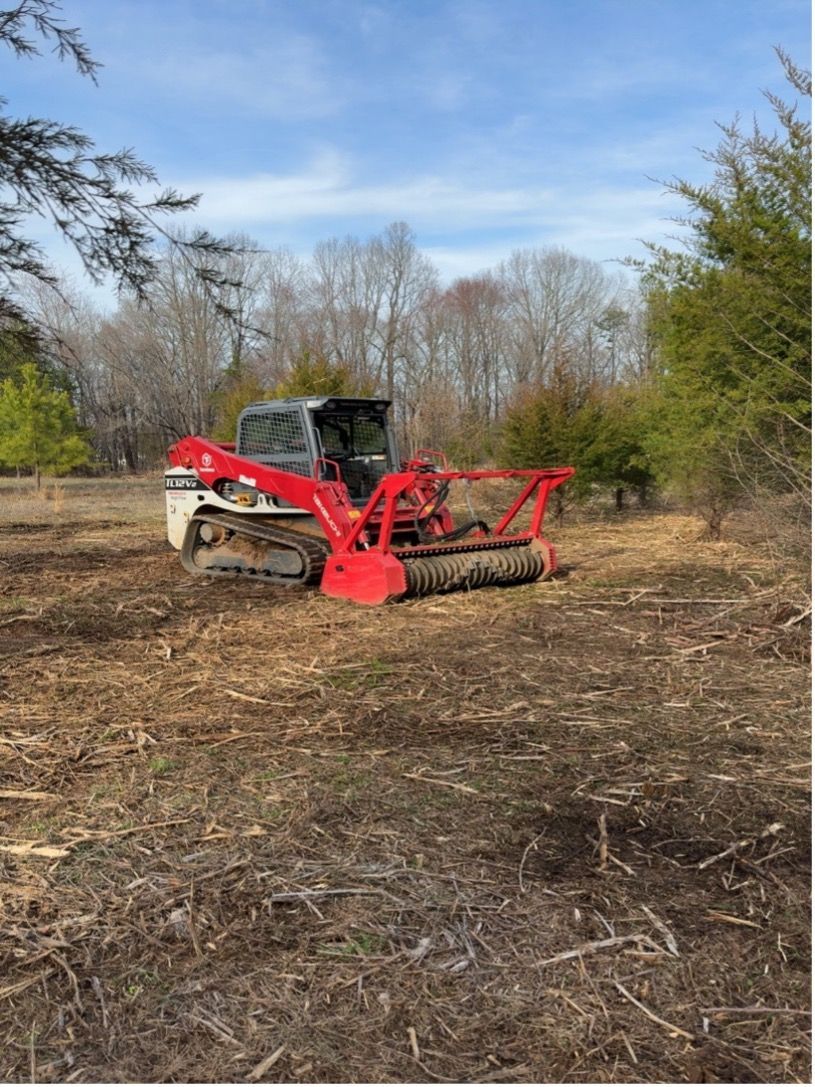 Red brush mower in a cleared field with trees and blue sky in the background
