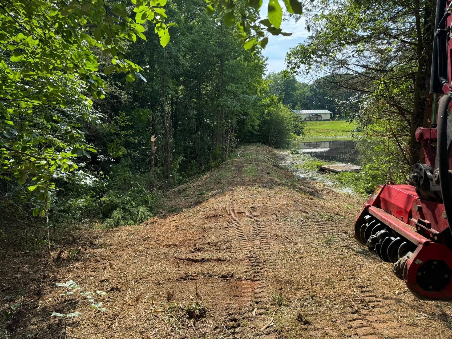 A freshly cleared dirt path through a wooded area, with a red machine in the foreground.