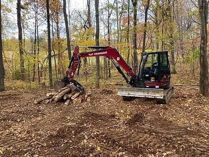 Red excavator in a wooded area, moving logs.