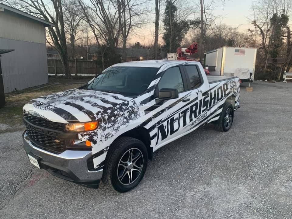 A black and white truck with the word nutrishop on the side is parked in a parking lot.