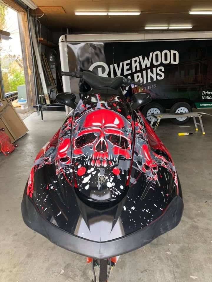 A red and black jet ski with a skull on it is parked in a garage.
