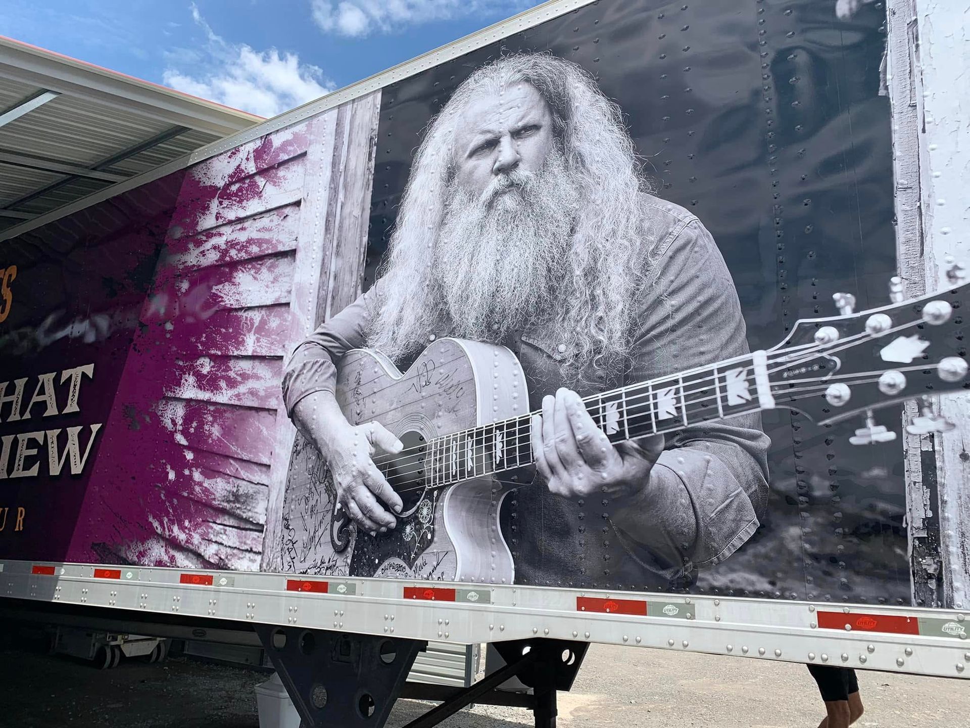 A man with a beard is playing a guitar on the side of a truck.