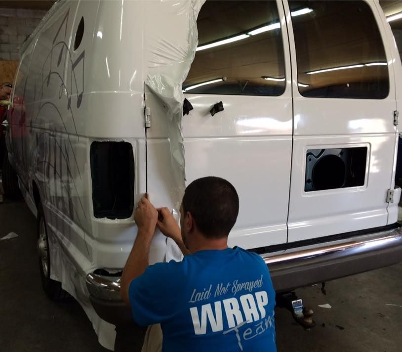 A man in a blue shirt that says wrap is wrapping a white van