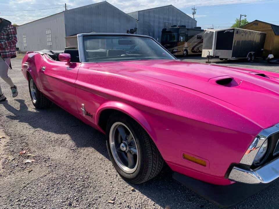 A pink mustang convertible is parked in a parking lot.
