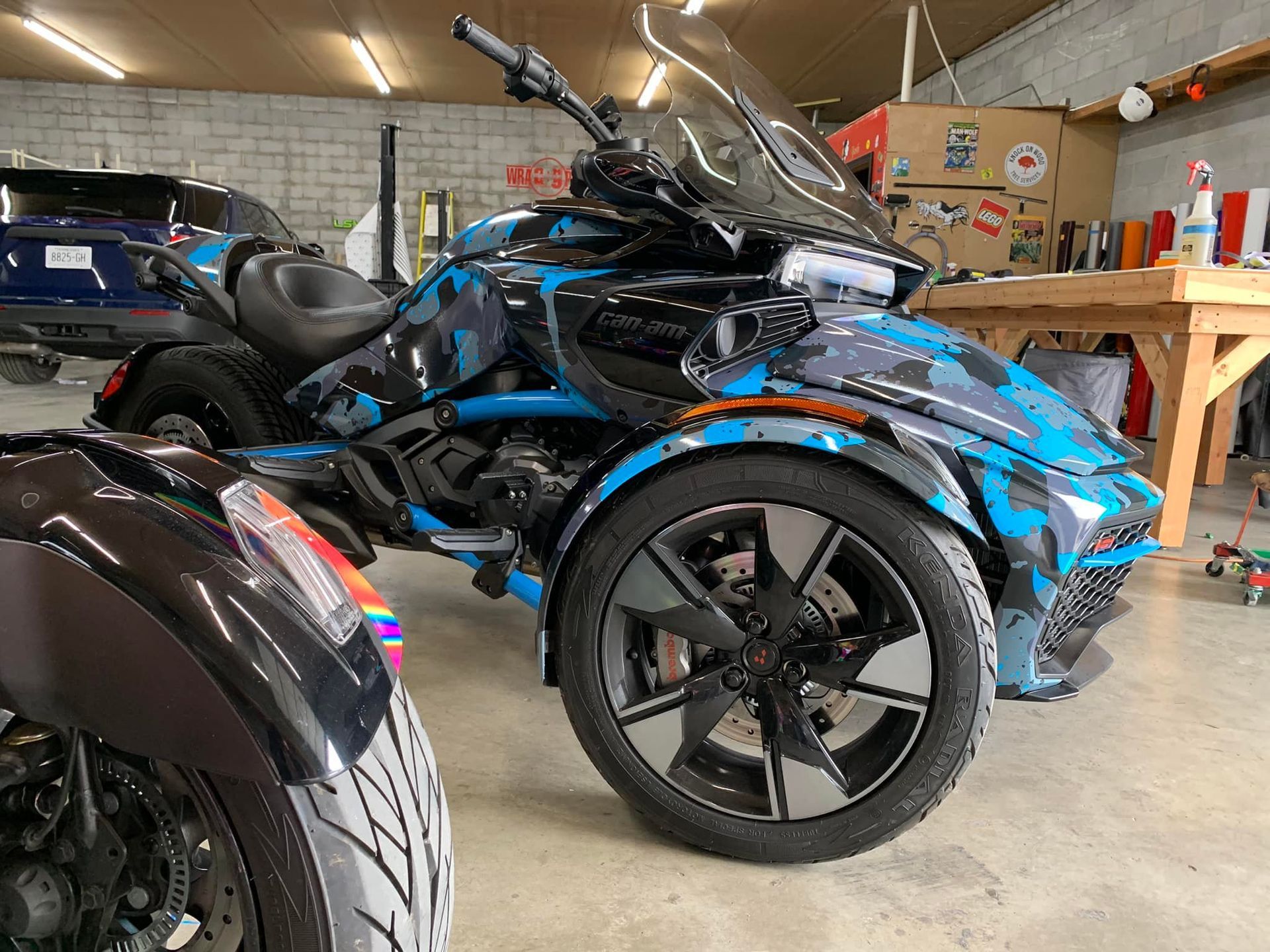 A blue and black motorcycle with three wheels is parked in a garage.